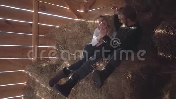 在寒冷的冬季谷仓里一对漂亮的年轻夫妇坐在干草上年轻的农民和妻子在一天工作后休息视频的预览图