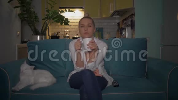 女孩喝咖啡茶和她的猫一起看电视4K视频的预览图