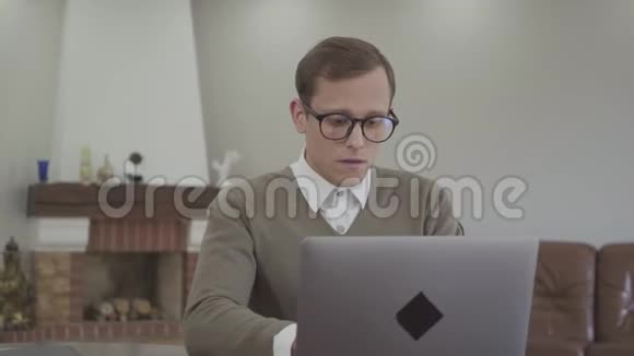肖像年轻忙碌严肃端庄戴眼镜的男人坐在家里的桌子上书在桌子上书呆子视频的预览图