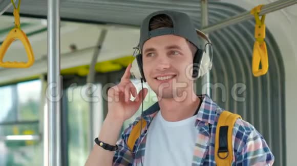 年轻的帅哥在公共交通工具中享受旅行站在现代电车上戴着耳机视频的预览图