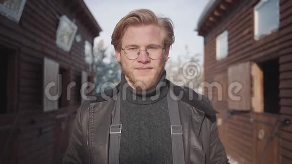 一个英俊的留胡子的家伙的肖像戴着一着温暖毛衣和夹克的眼镜慢动作视频的预览图