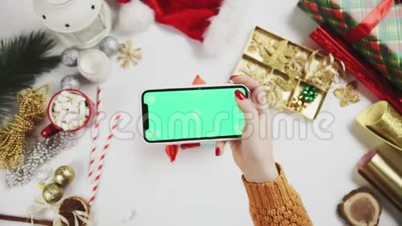 女士双手拍照圣诞礼物在白色桌子上绿屏手机显示视频的预览图