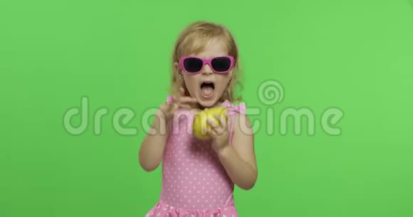 穿着粉红色泳衣和太阳镜的孩子吃一个绿色的梨色度键视频的预览图