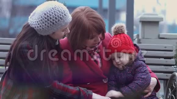 一家三代微笑的妇女坐在城市公园的长凳上拥抱家庭观念妈妈视频的预览图