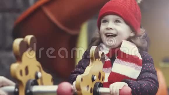 快乐的笑女34岁穿着温暖的衣服在明亮多彩的操场上摇杆玩耍视频的预览图