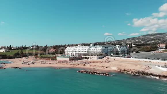 在阳光明媚的多风天气里以蓝色的海水和波浪俯瞰塞浦路斯的珊瑚湾沙滩在干净的沙地上飞行的视频的预览图