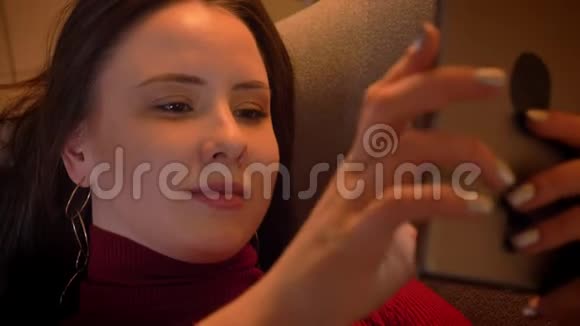 年轻迷人的白种人女性在平板电脑上发短信躺在舒适的沙发上微笑特写镜头视频的预览图