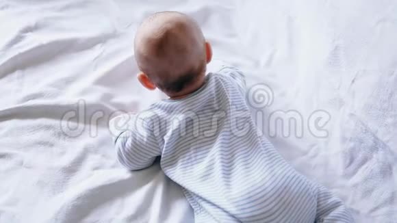 可爱快乐的4个月大的男孩躺在白色的床上玩耍视频的预览图