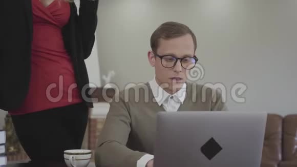 肖像年轻端庄戴眼镜的男人坐在家里的桌子上用笔记本电脑工作一个美丽的女人视频的预览图