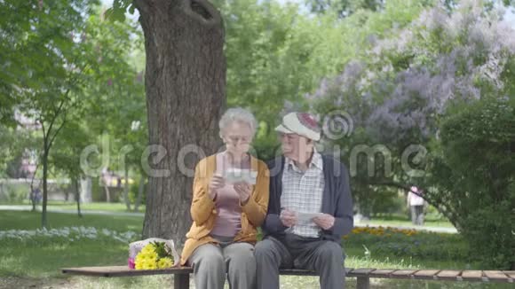肖像可爱的成年夫妇看着老照片回忆着坐在公园长凳上的快乐时刻成熟的夫妻视频的预览图