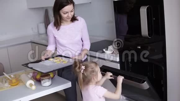 快乐妈妈教女儿在厨房做饭当女孩打开烤箱时妈妈拿着一个托盘上面放着饼干视频的预览图