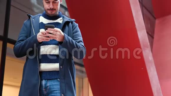 英俊的年轻人站在办公楼外在工作中休息时使用手机视频的预览图