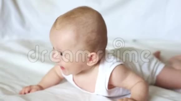 可爱快乐的6个月小男孩躺在白色的床上玩耍视频的预览图