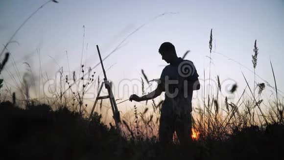 一位男性艺术家在自然景观中描绘日落景观的剪影视频的预览图