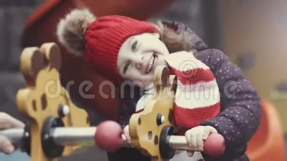 快乐的笑女34岁穿着温暖的衣服在明亮多彩的操场上摇杆玩耍视频的预览图