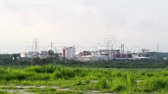 清晨一家化工厂在一片绿色的稻田中间烟囱冒烟工厂的管道污染视频的预览图