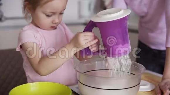 小可爱的女儿正在厨房里帮她的母亲在碗里加入面粉和筛子并混合配料视频的预览图