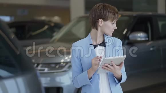 一幅自信的漂亮女人穿着时尚西装在车展上用平板电脑检查汽车的肖像女士检查视频的预览图