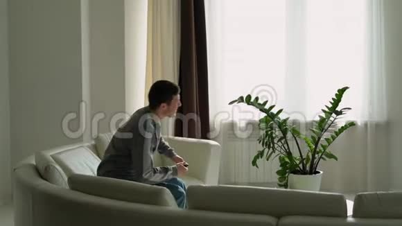 一个年轻人坐在沙发上打开电视遥控器视频的预览图