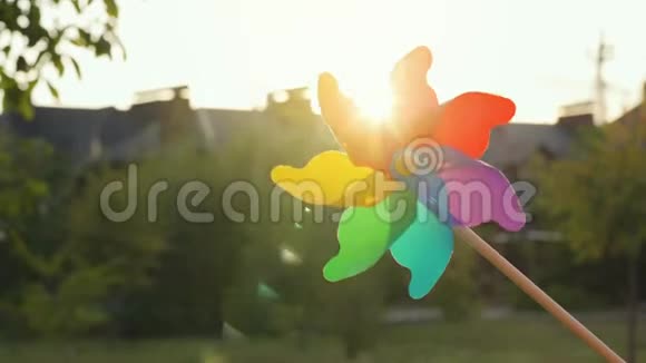 塑料彩虹风车在模糊的房子和日落的背景上旋转郊区概念视频的预览图