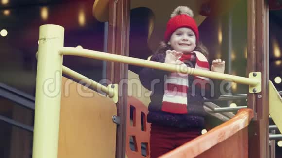 快乐的微笑女孩34岁穿着温暖的衣服站在明亮多彩的操场上的滑梯上视频的预览图