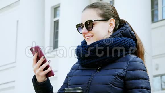 城市里一位戴着智能手机喝咖啡的眼镜的年轻女子的特写照片视频的预览图