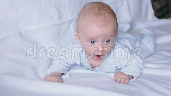 可爱快乐的4个月大的男孩躺在白色的床上玩耍视频的预览图