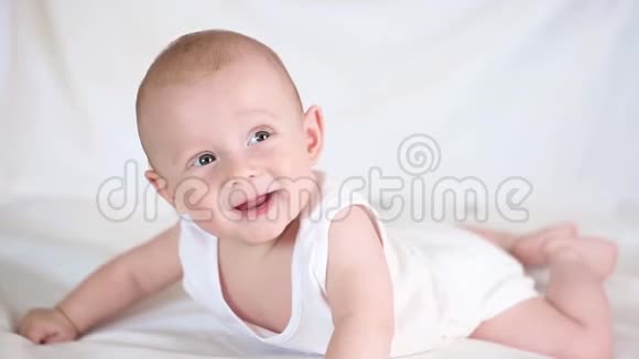 可爱快乐6个月小男孩躺着玩在白色的床上视频的预览图