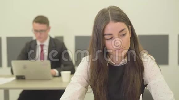 一位穿着正式服装的体贴的年轻女士坐在办公室的前台而她的男性同事则坐在办公室的画像中视频的预览图