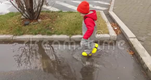 穿黄靴子的男孩穿过水坑视频的预览图