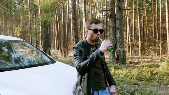 醉汉在汽车附近喝啤酒在大自然中扔出一瓶视频的预览图