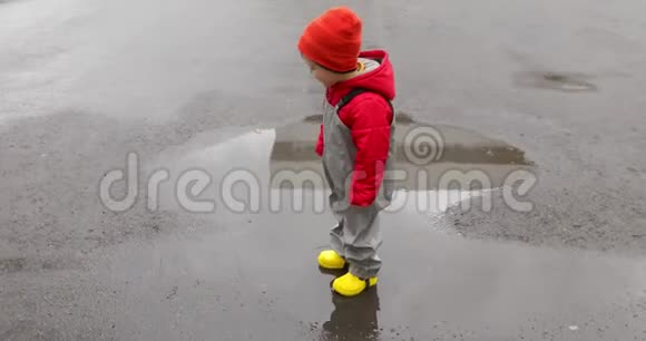 穿黄靴子的男孩穿过水坑视频的预览图