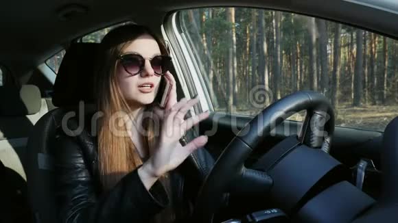 时髦的女人在手机上说话坐在汽车的轮子上视频的预览图