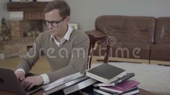 一个穿着眼镜的年轻男子坐在办公室的木桌旁手提电脑视频的预览图
