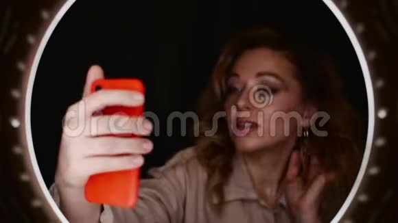 美妆博主女性在环光面前手持智能手机自拍视频的预览图