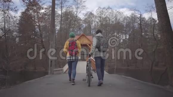 两名游客背着背包在公园的桥上散步男人牵着自行车女人进来视频的预览图