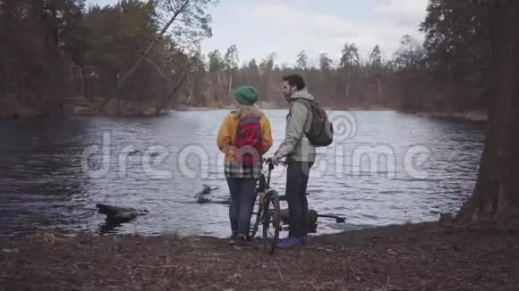 年轻的一对游客站在河岸上背着背包男人拿着自行车女人进来视频的预览图