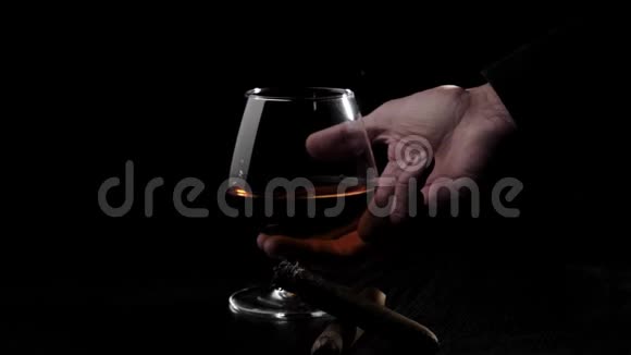 豪华白兰地带有干邑和两支雪茄的玻璃杯在黑色背景下的黑色桌子上旋转手拿一杯白兰地视频的预览图