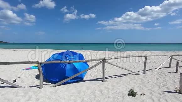 被遗弃的白色海滩带着一把蓝色的海滩伞从后面看到在蓝色的大海和蓝色的背景下在风中飘扬视频的预览图