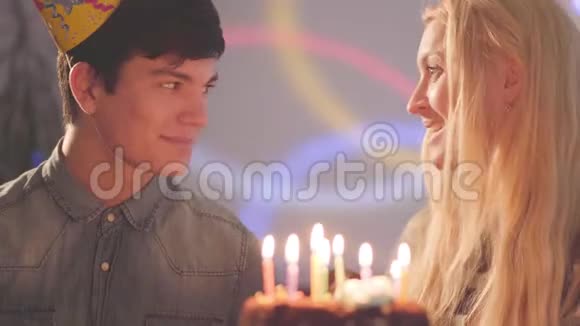 肖像金发女孩和英俊的男人戴着生日帽坐在蛋糕前拿着蜡烛女人过生日视频的预览图