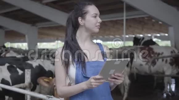 奶牛场年轻漂亮女工的肖像用她的平板电脑检查工作过程积极的农民视频的预览图