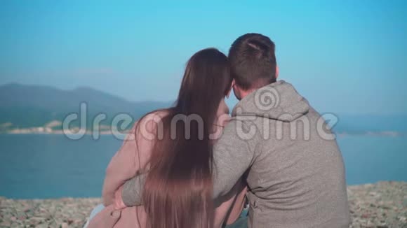 一个年轻的女孩和一个男人坐在海滩上拥抱在春天那个女孩和那个相框里的家伙旋转视频的预览图