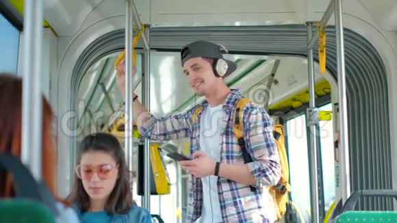 年轻的帅哥在公共交通工具中享受旅行站在现代电车上戴着耳机视频的预览图