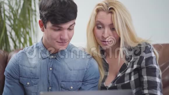可爱的一对夫妇坐在家里的笔记本电脑前一个黑发男人和金发女人讨论关于视频的预览图