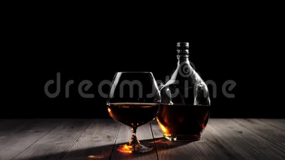 豪华白兰地一个圆形瓶子里的金色干邑站在一个玻璃旁边木桌上放着干邑背景是黑色的视频的预览图