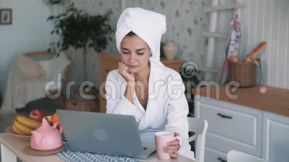 穿白色浴袍的女孩头上有毛巾在笔记本电脑上视频聊天慢动作视频的预览图