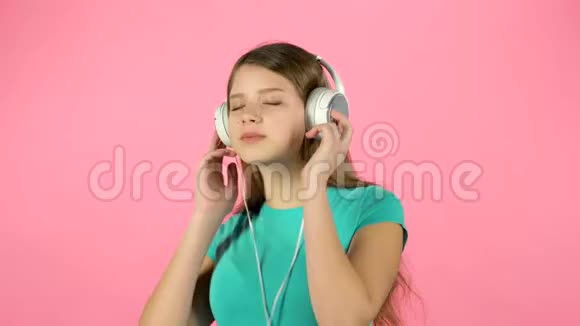 女孩在粉红色背景下用白色大耳机听音乐和跳舞视频的预览图