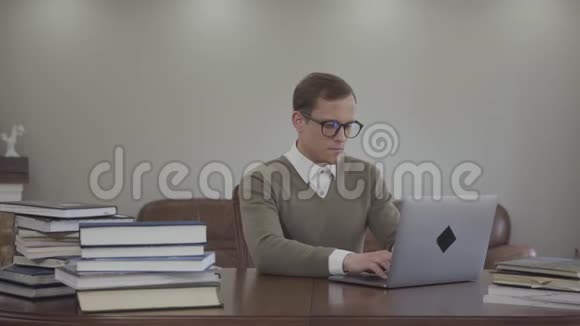 肖像可爱的男人戴着眼镜坐在办公室的木桌旁许多书都在桌子上可爱的书呆子视频的预览图