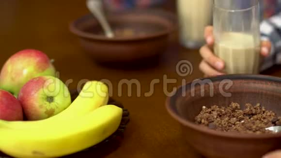 孩子们用特写的手从碗里的杯子里倒牛奶里面放着麦片愉快的友好家庭享受早餐视频的预览图