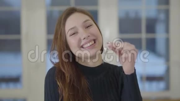 一个快乐可爱微笑的女人的肖像向相机展示一所新房子或公寓的钥匙广告视频的预览图